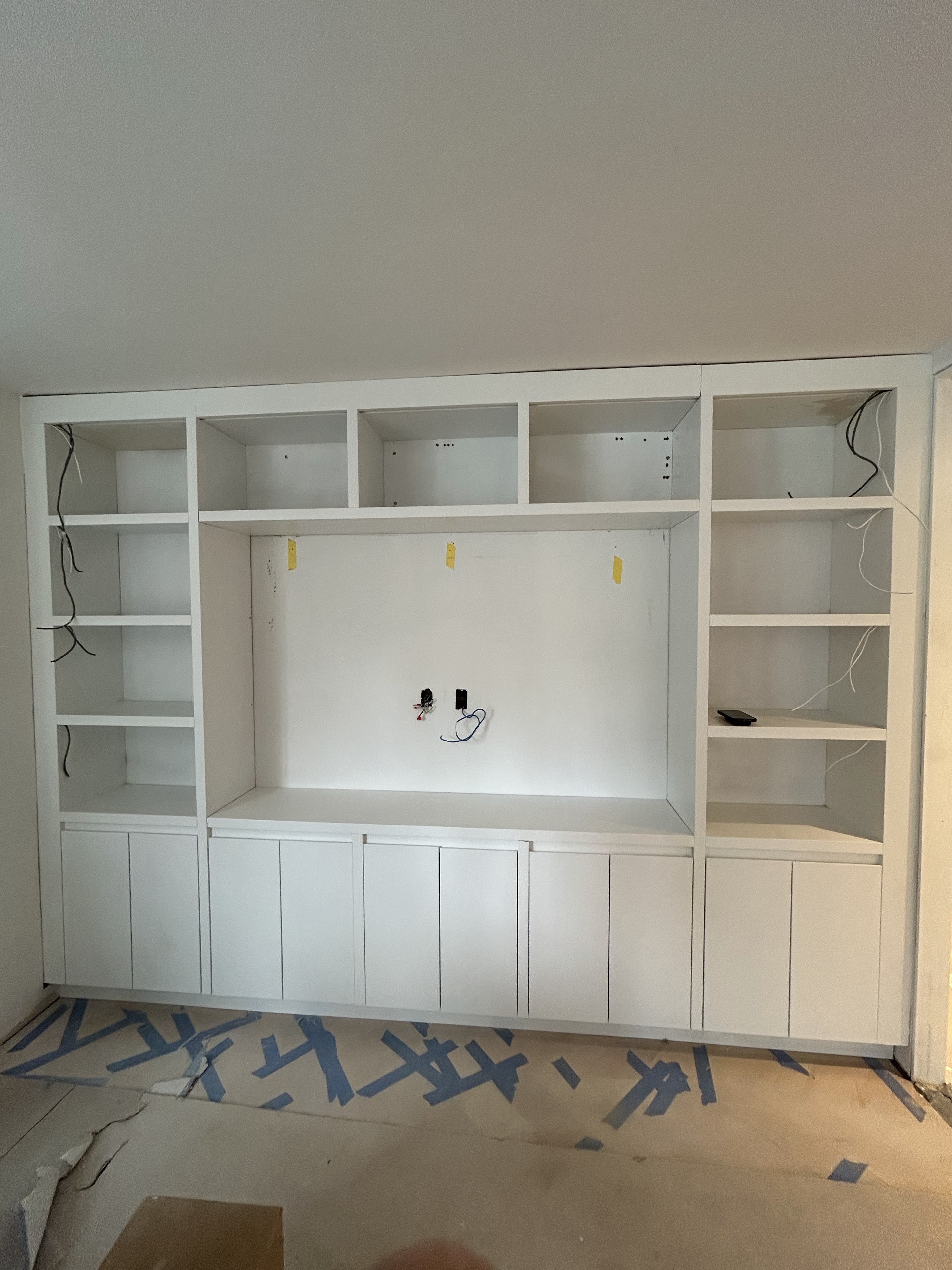 White custom media wall with shelves and lower cabinets during installation