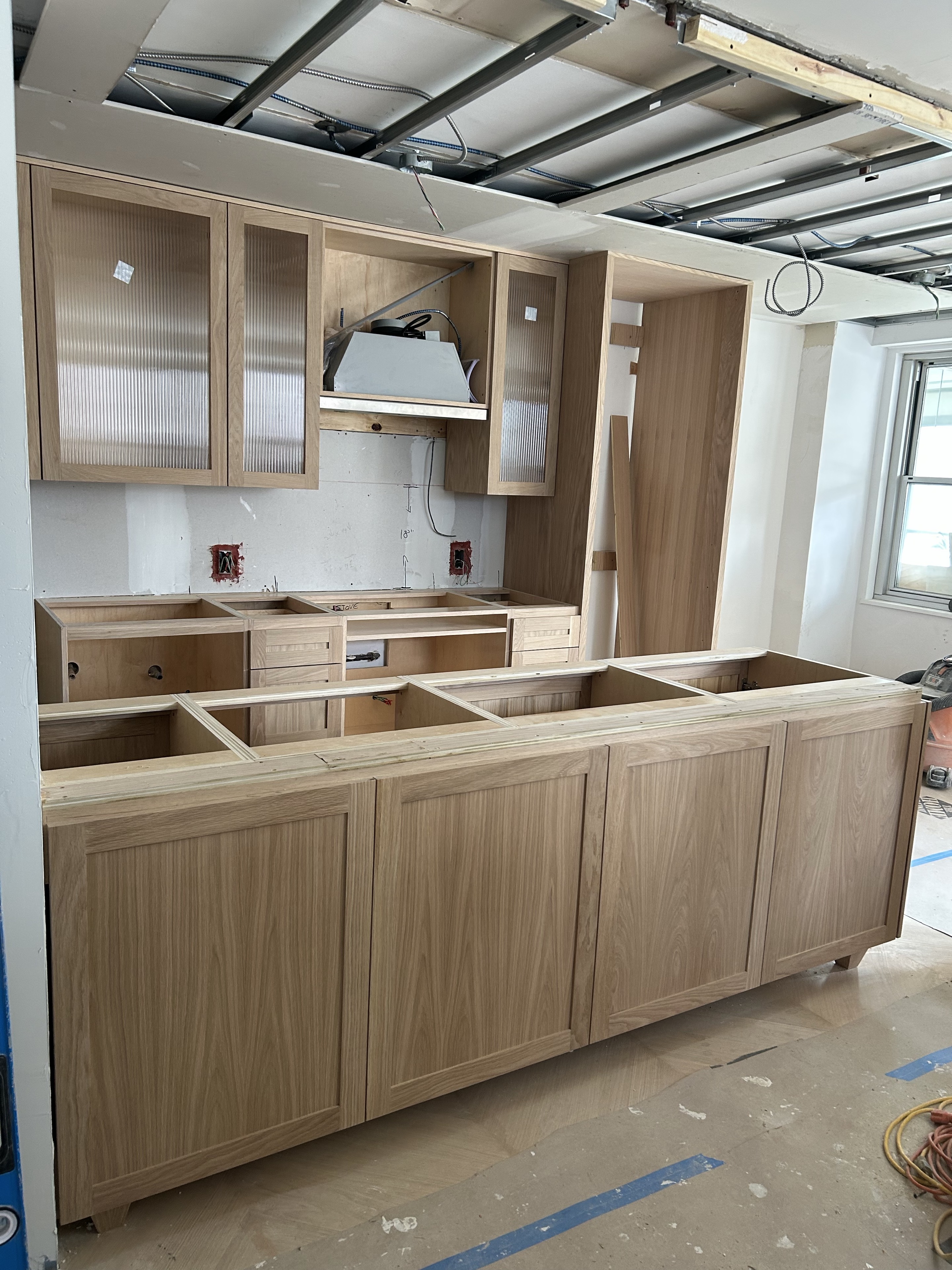 Oak kitchen cabinetry during installation, with unfinished ceiling visible